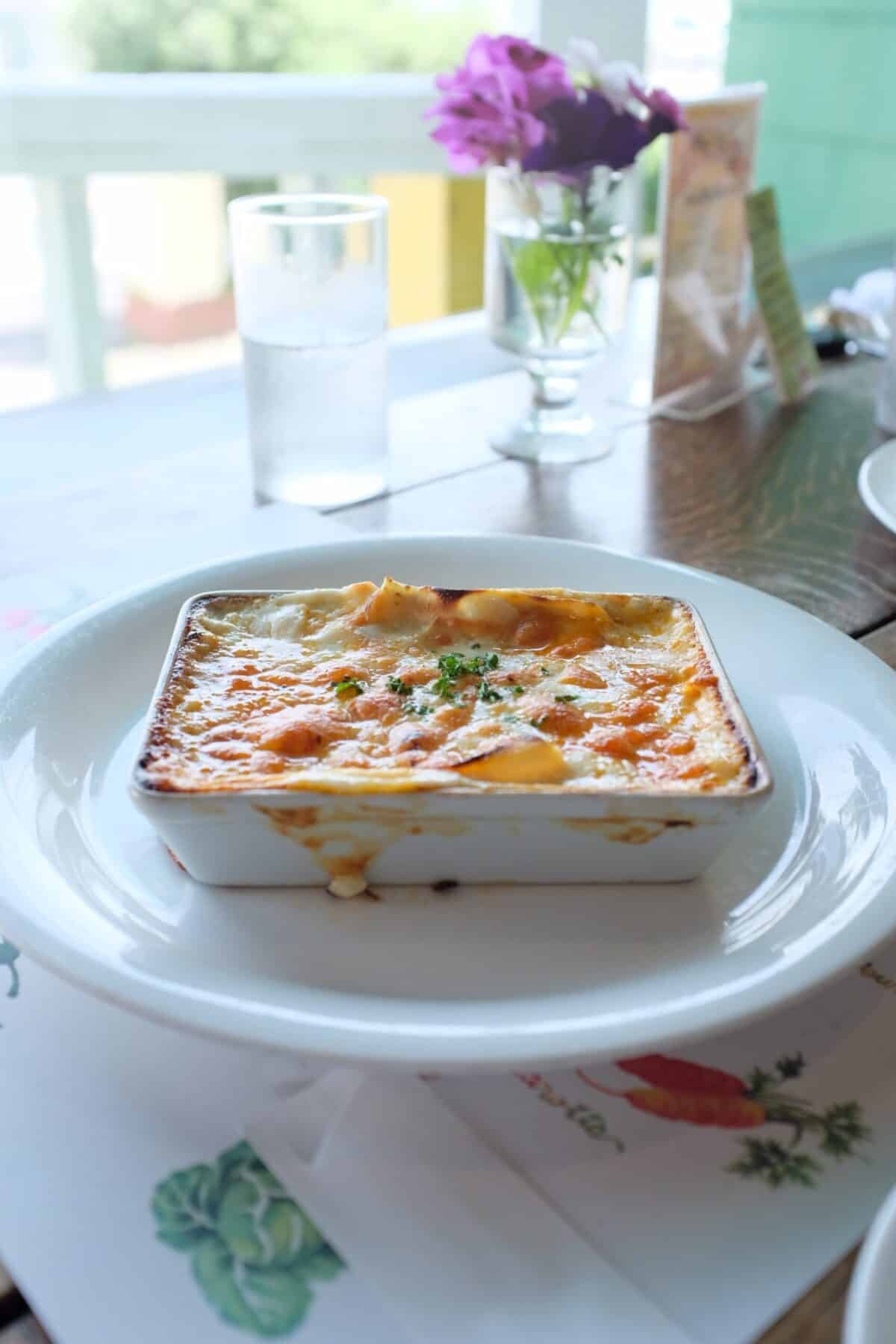 A breakfast casserole on a large white charger plate with flowers in the background.