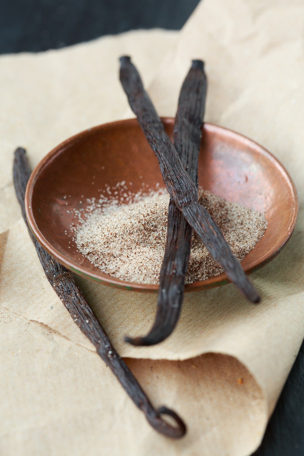 3 vanilla beans sitting in a brown bowl.