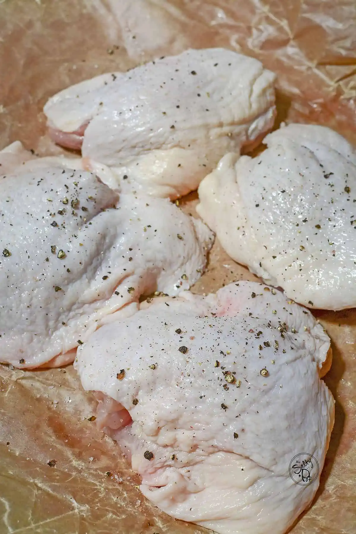 Chicken thighs that are raw, sitting on brown butcher paper, that have been seasoned.
