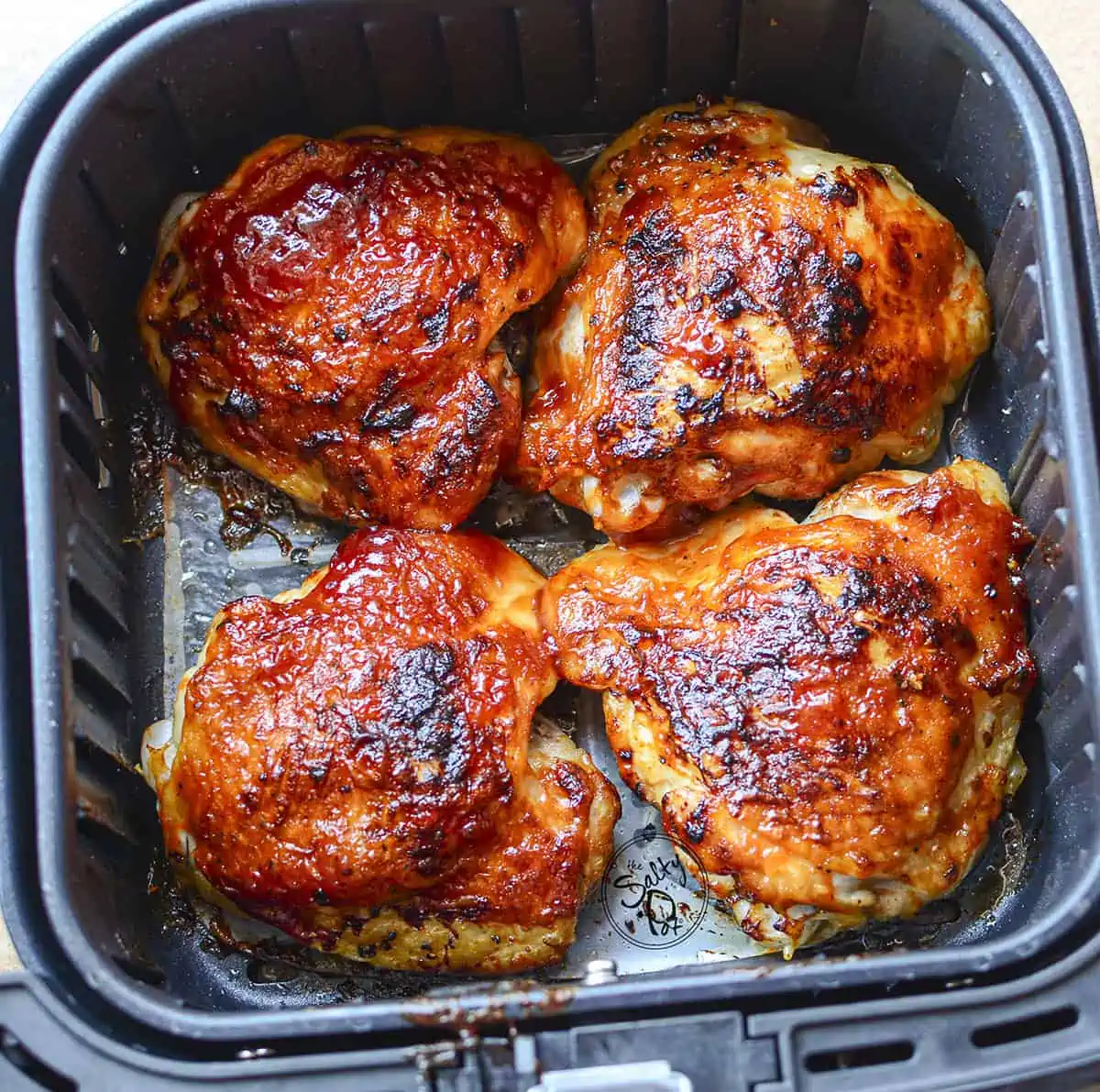 4 fully cooked chicken thighs with crispy skin inside the air fryer basket.
