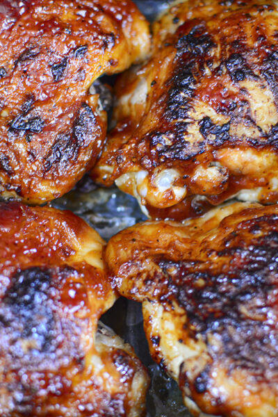 Four chicken thighs that have been cooked and sauced resting in the basket of the air fryer.