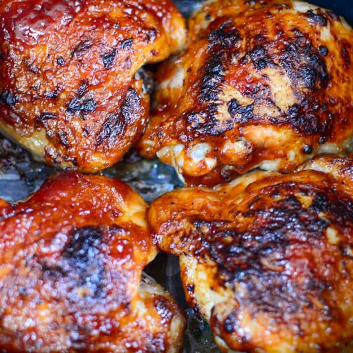 Four chicken thighs that have been cooked and sauced resting in the basket of the air fryer.