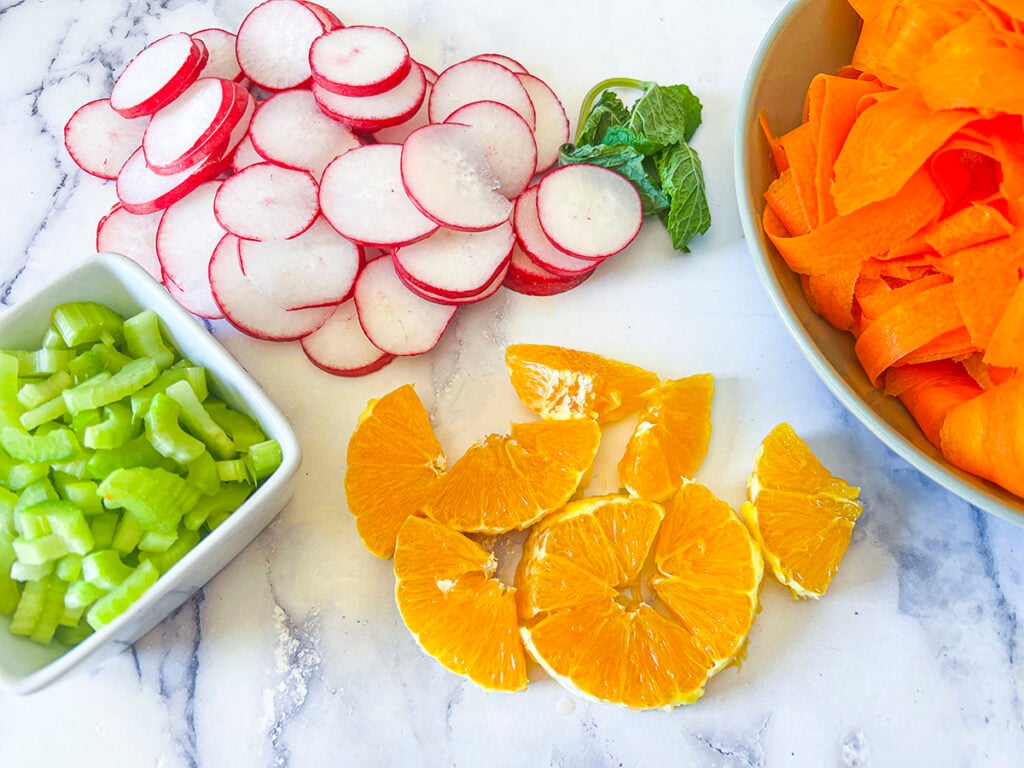 Sliced radish, celery, carrot and orange segments on a marble cutting board.