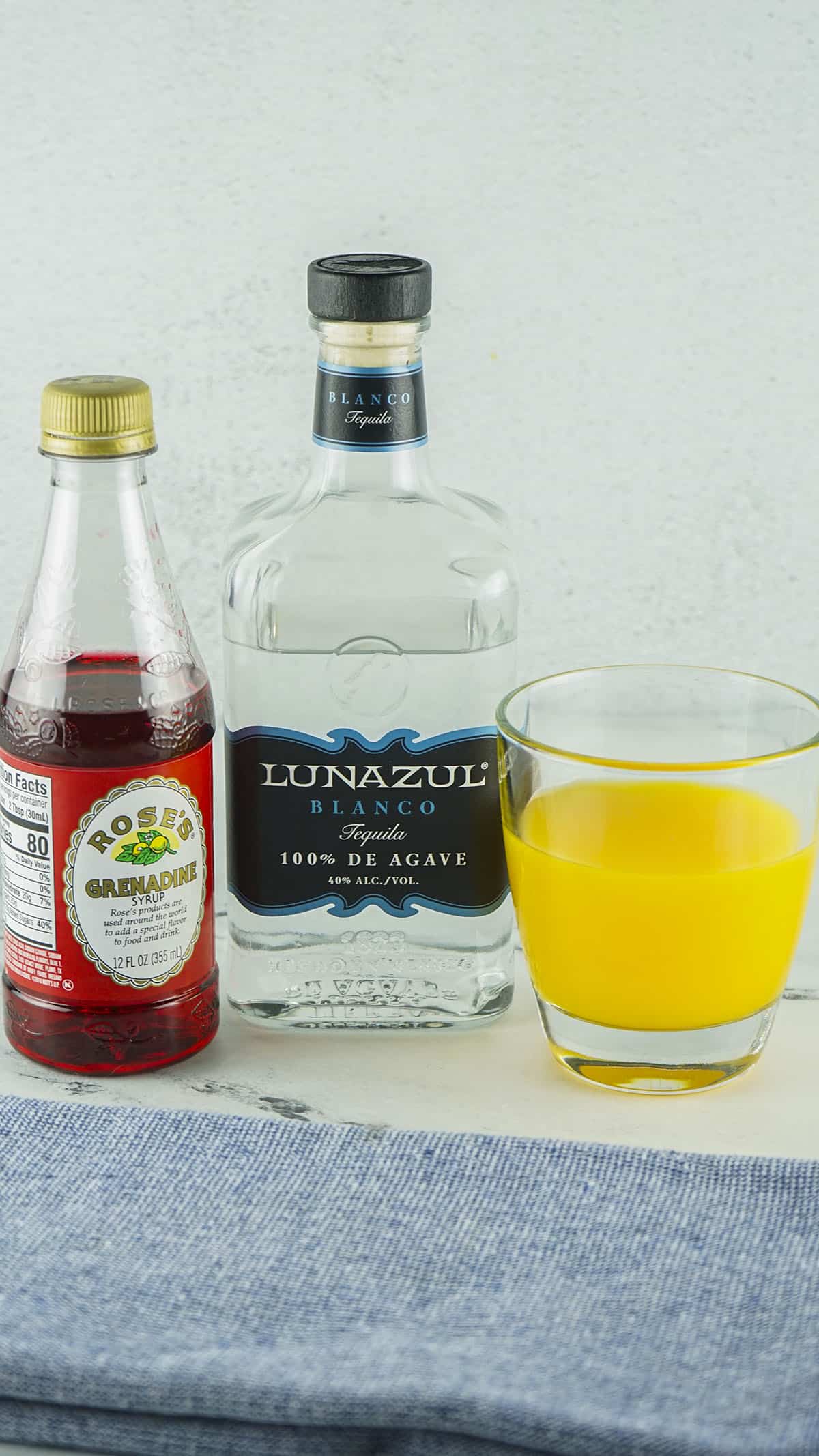 The ingredients needed to make the cocktail. Grenadine syrup is featured left, then tequila and orange juice.