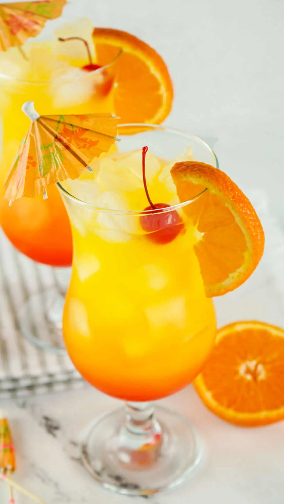Two tropical tequila sunset drinks garnished with cherries and orange slices.