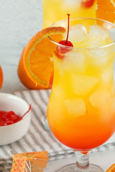A Tequila Sunset Cocktail garnished with sweet cherries and oranges in a tall glass.