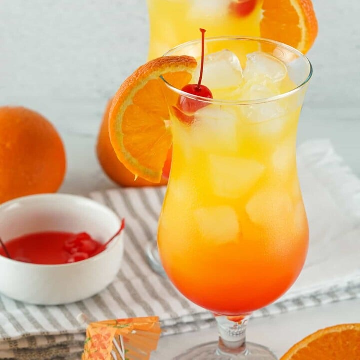 A Tequila Sunset Cocktail garnished with sweet cherries and oranges in a tall glass.
