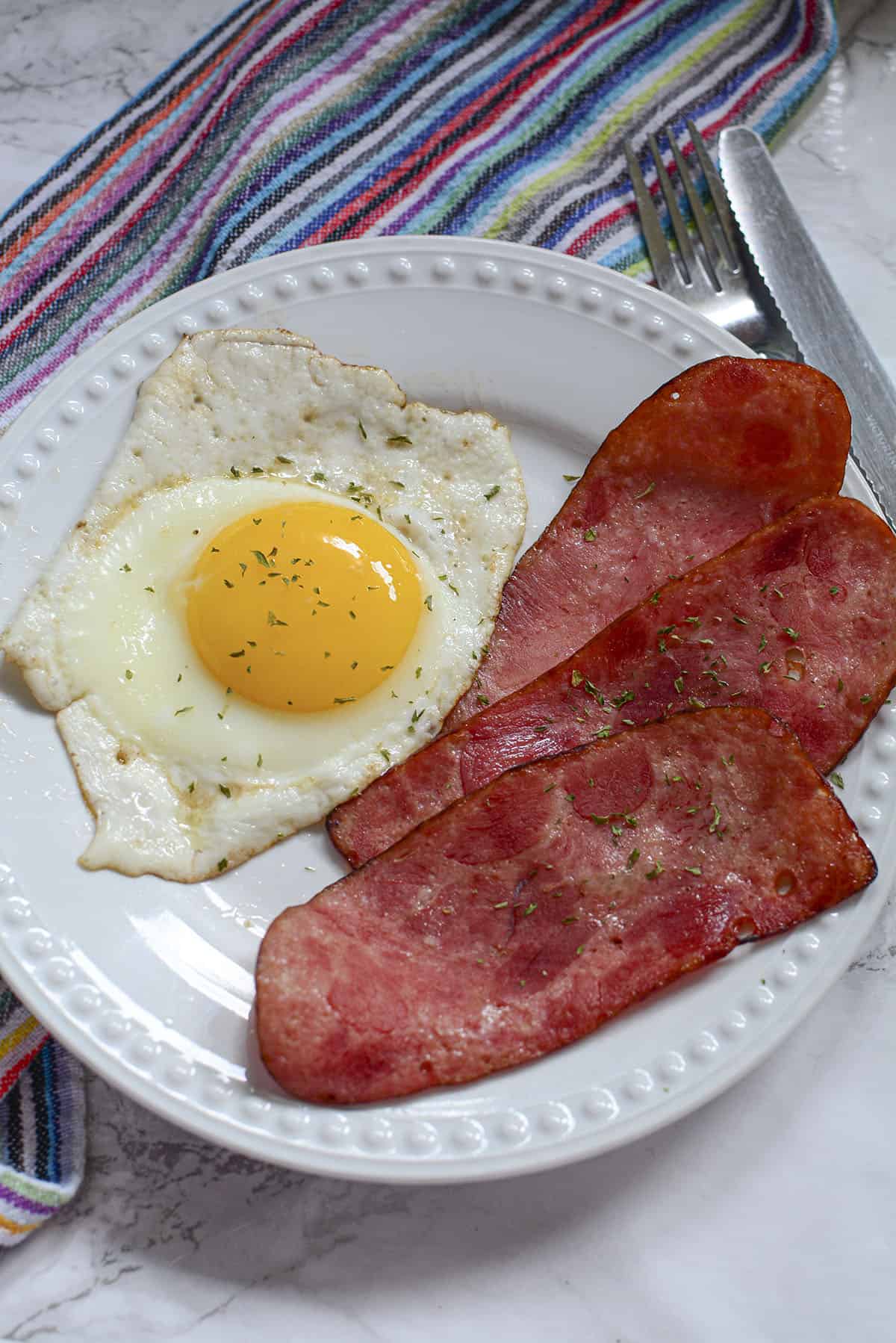 Three cooked turkey bacon slices on a white plate next to one cooked sunny side up egg.