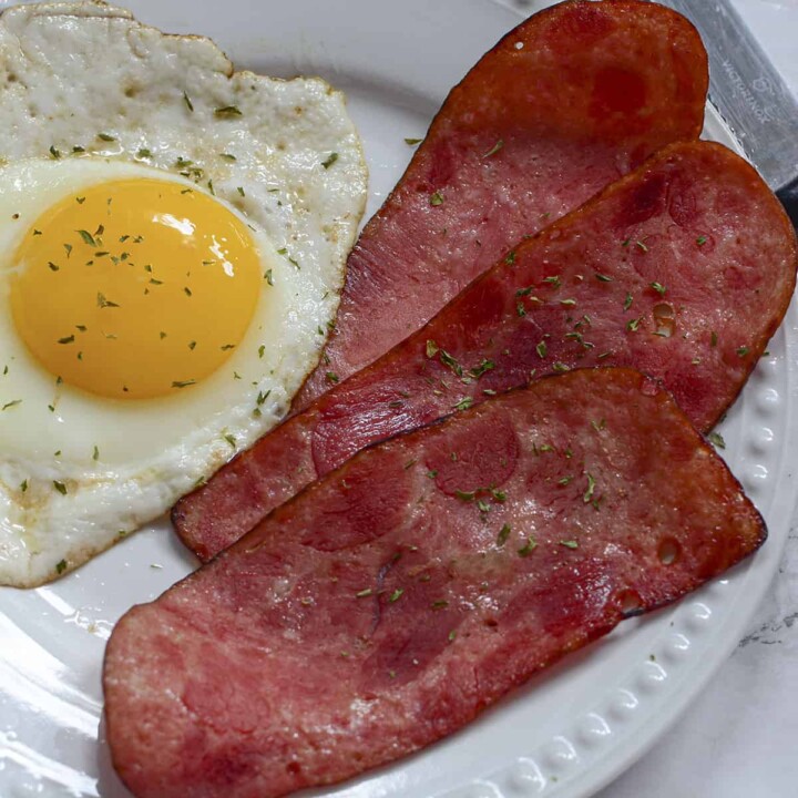 Three strips of turkey bacon on a plate next to one egg.