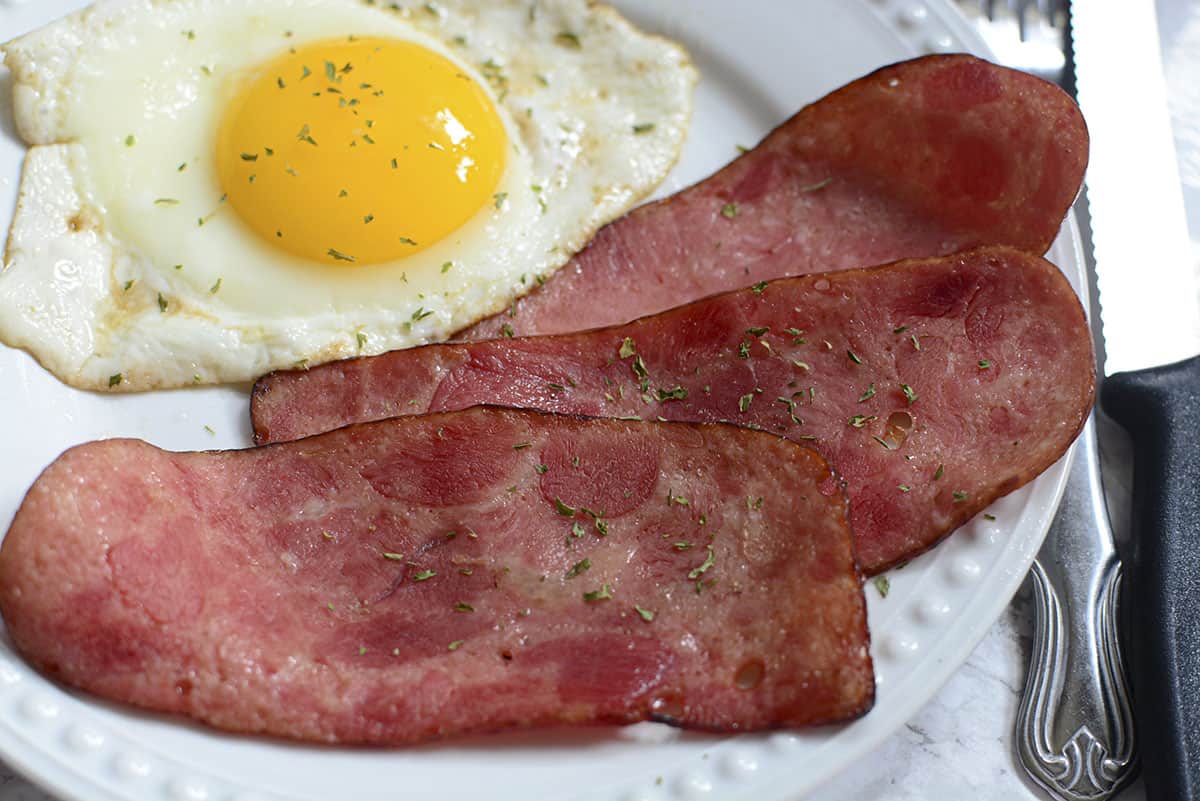 Turkey bacon on a plate with an egg and a fork and knife.