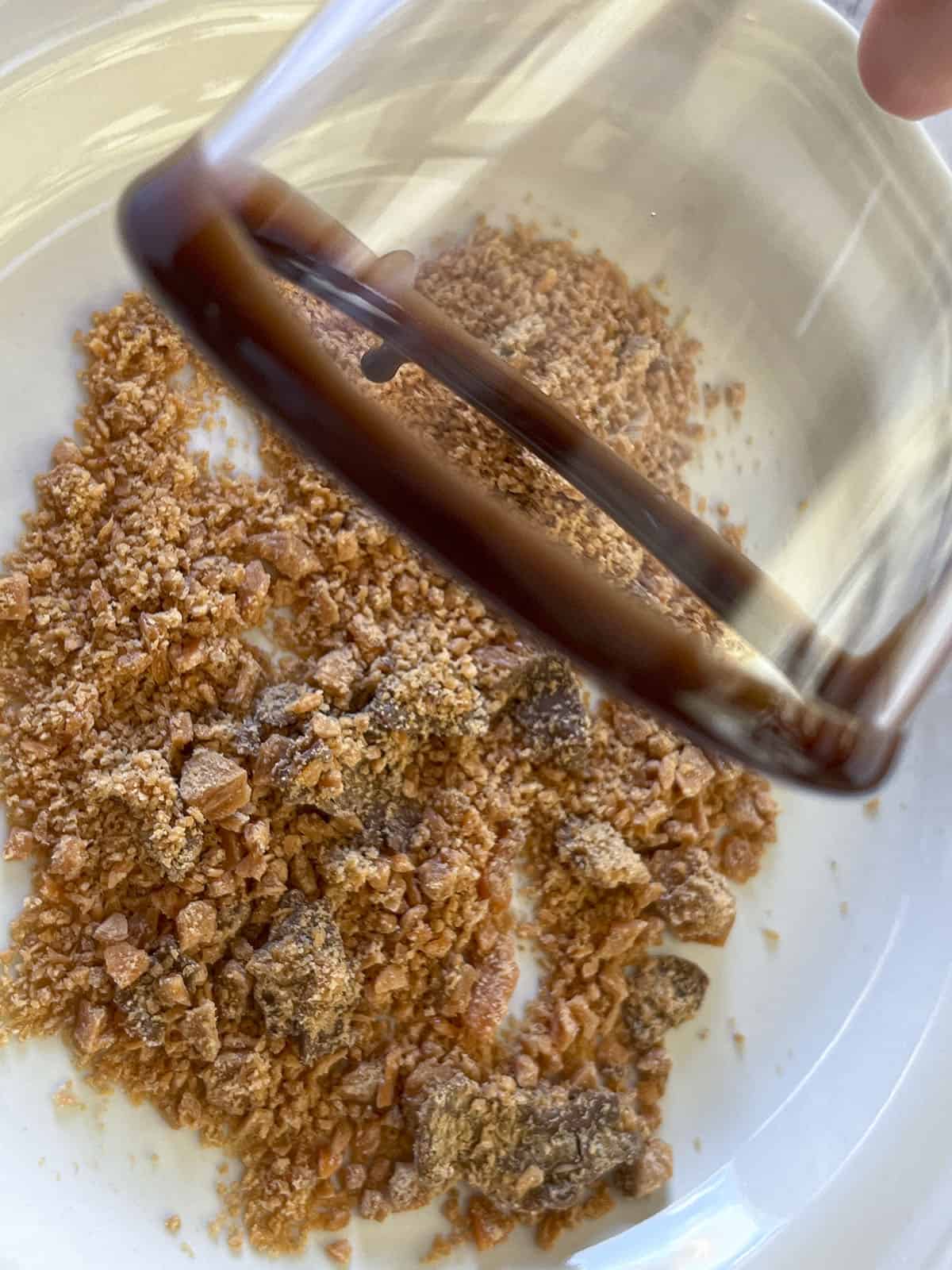 The syrup rimmed shotglass being dipped into crushed butterfinger candy.