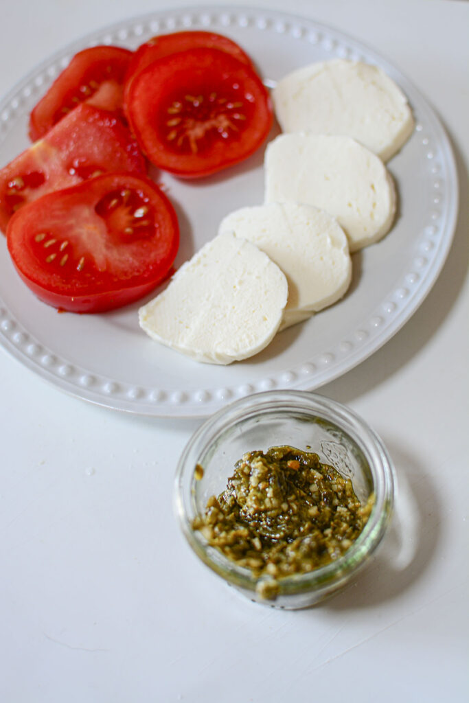 Sliced tomatoes, sliced fresh mozzarella cheese and pesto are featured ingredients on a plate.