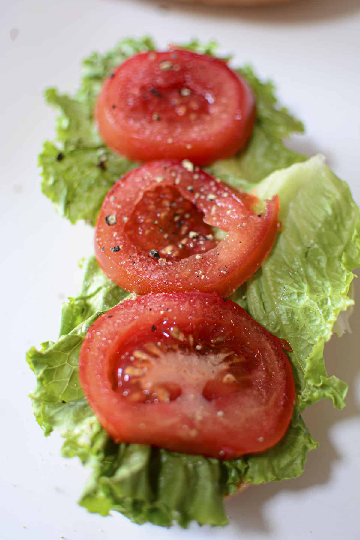 Tomatoes seasoned with salt and pepper are on top of the romaine lettuce.