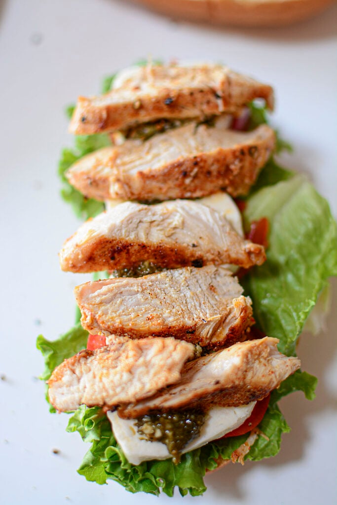 The cooked chicken is placed on the very top of all the ingredients for the sandwich.