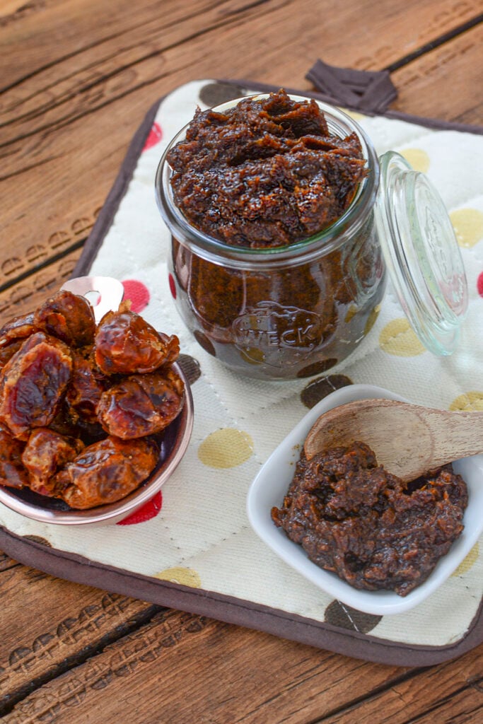 Date paste pictured at the top with a small amount of paste in a white bowl. On the left is a whole bowl of dried dates. 