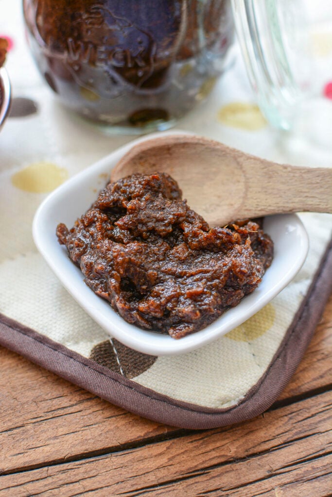 A white small bowl with a wooden spoon, scooping some date paste.