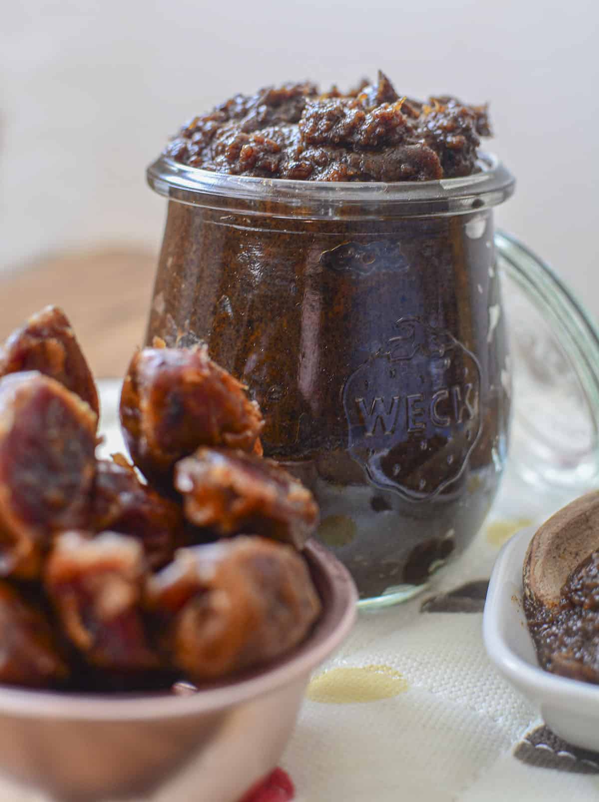 Date paste in a glass jar with whole dates on the table in front of it. 