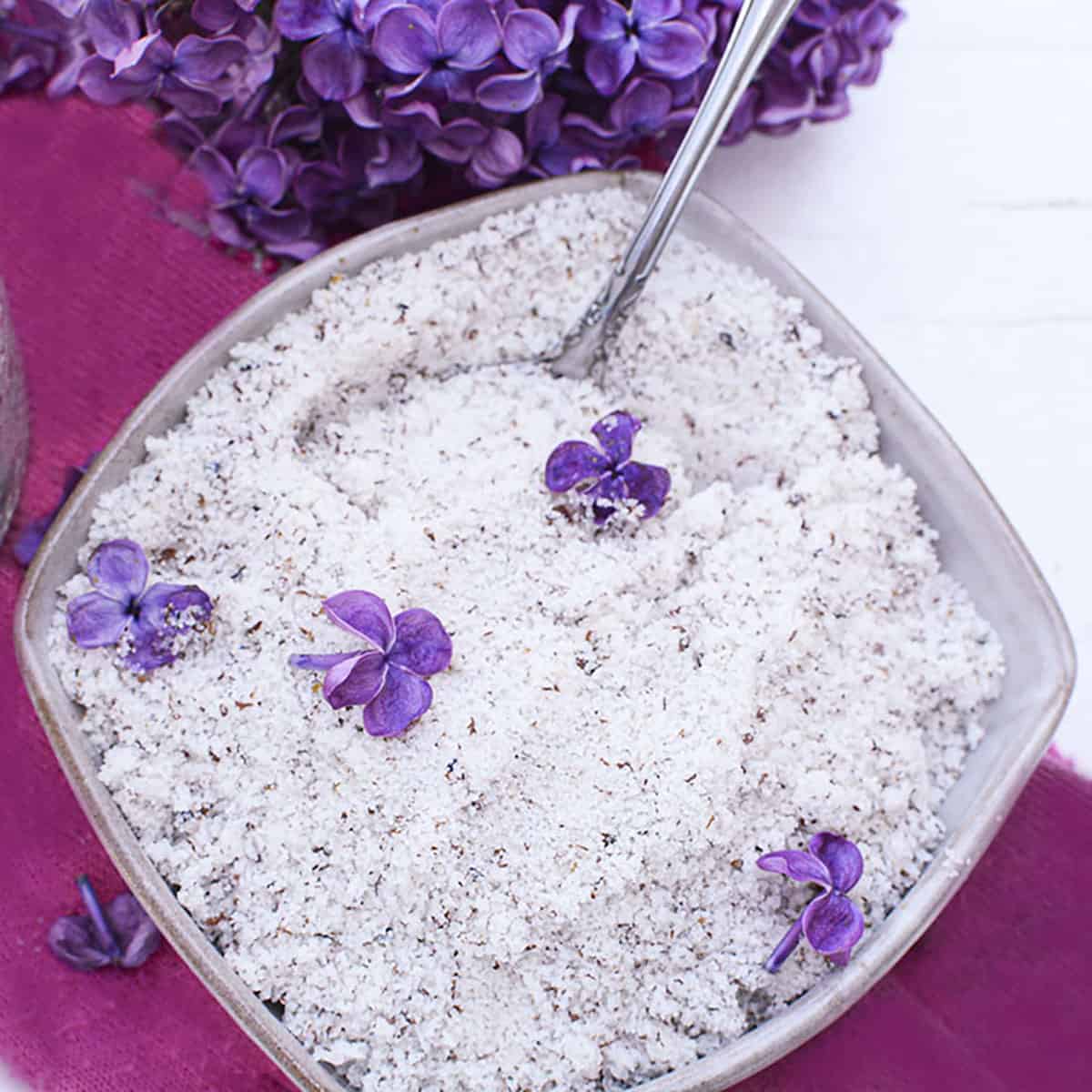 Lilac sugar in a bowl on a purple sloth with lilacs at the top.