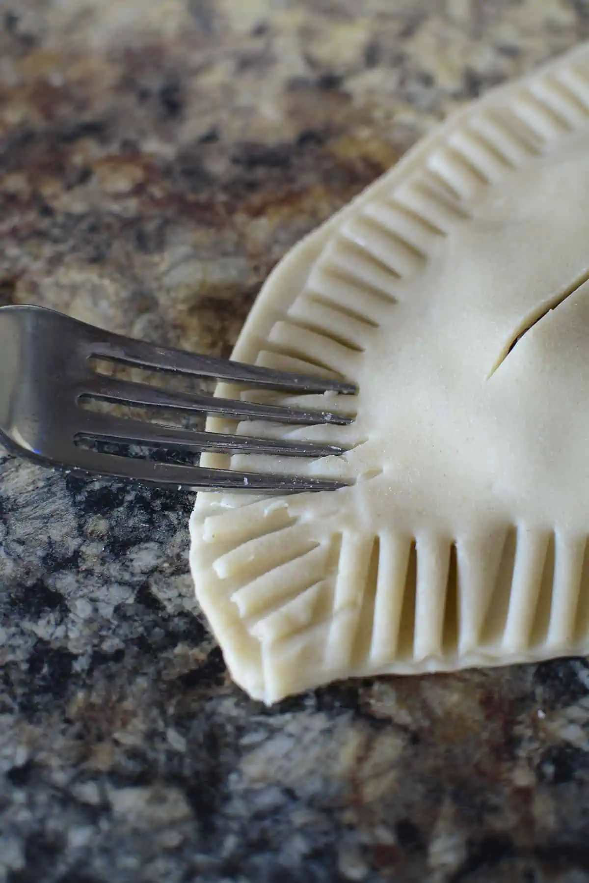 A fork stamping the two pieces of pastry together to seal it.