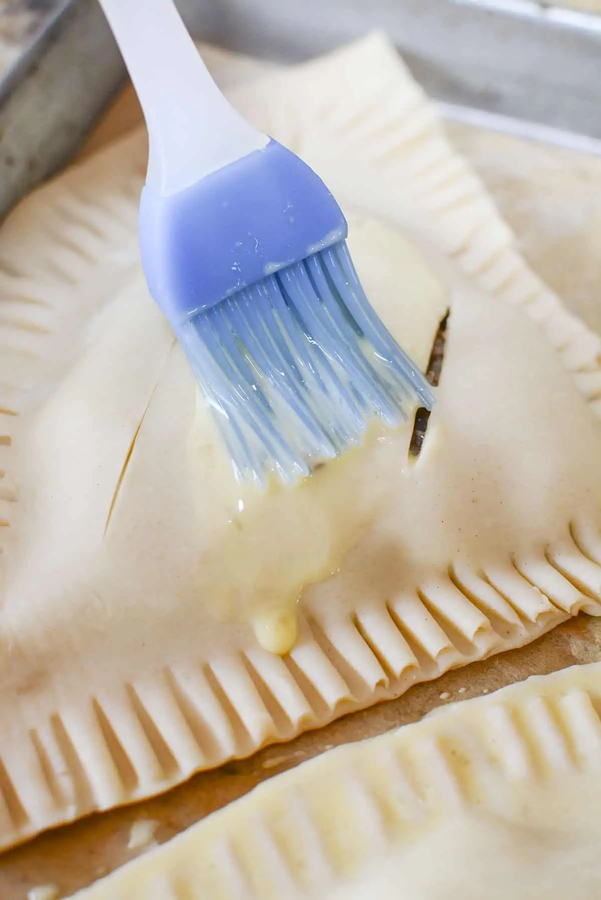 A blue silicone brush brushing on the egg wash.