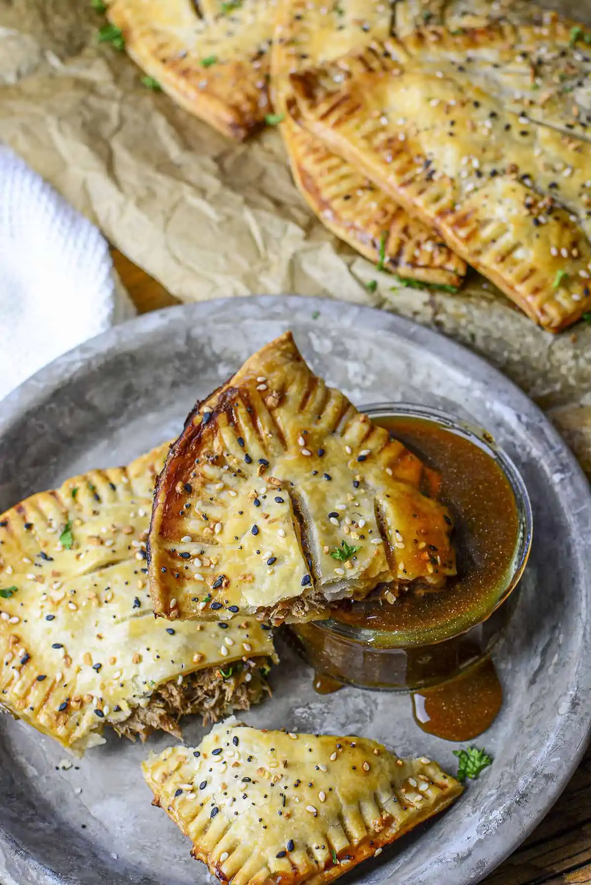 A beef hot pocket portion that is being dipped into savory beef gravy, on a tin plate.