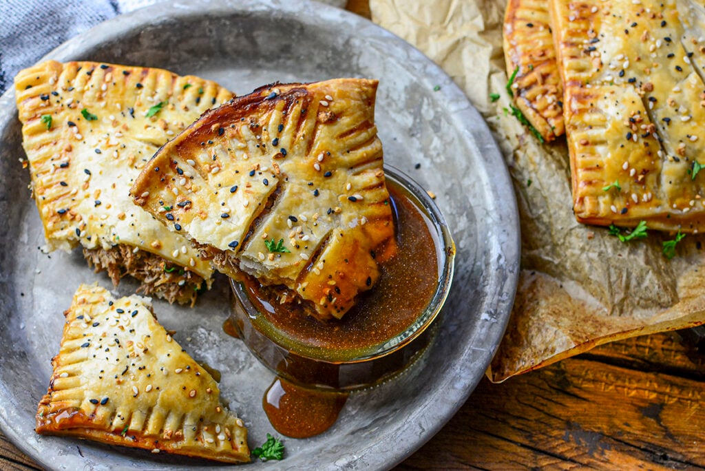 Beef hot pockets on a pie plate, one being dunked into gravy.