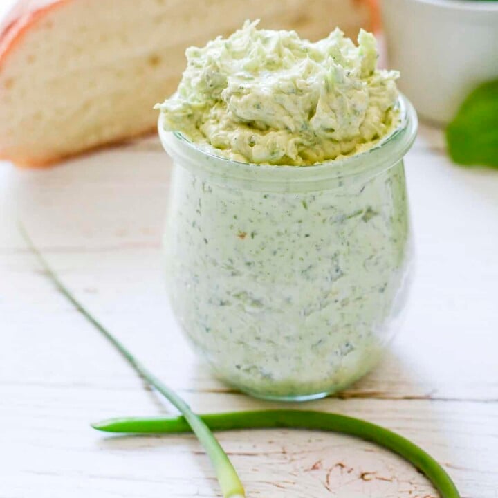 Garlic scape butter in a glass jar with one fresh scape folded on the table in front of it.