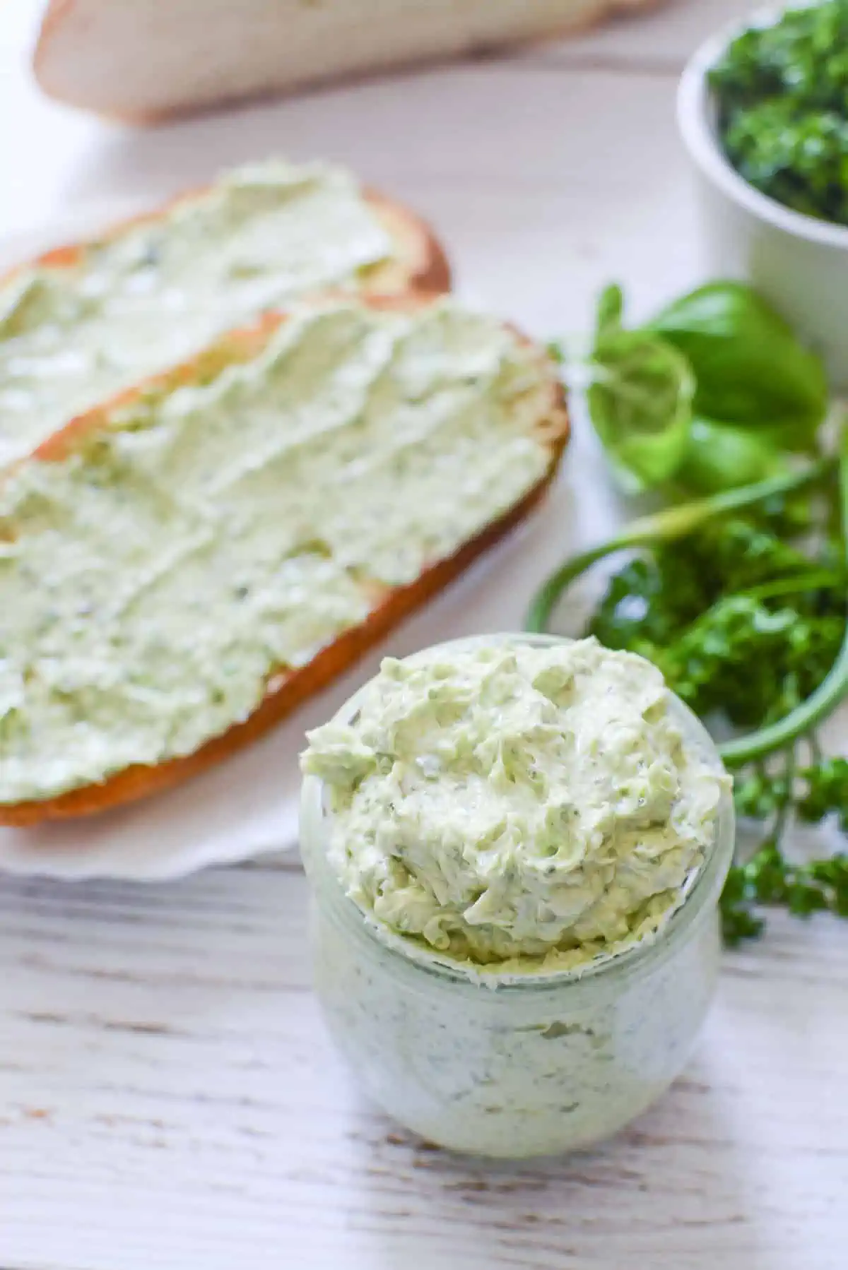 Garlic butter in a glass container with buttered toast in the background on the left.