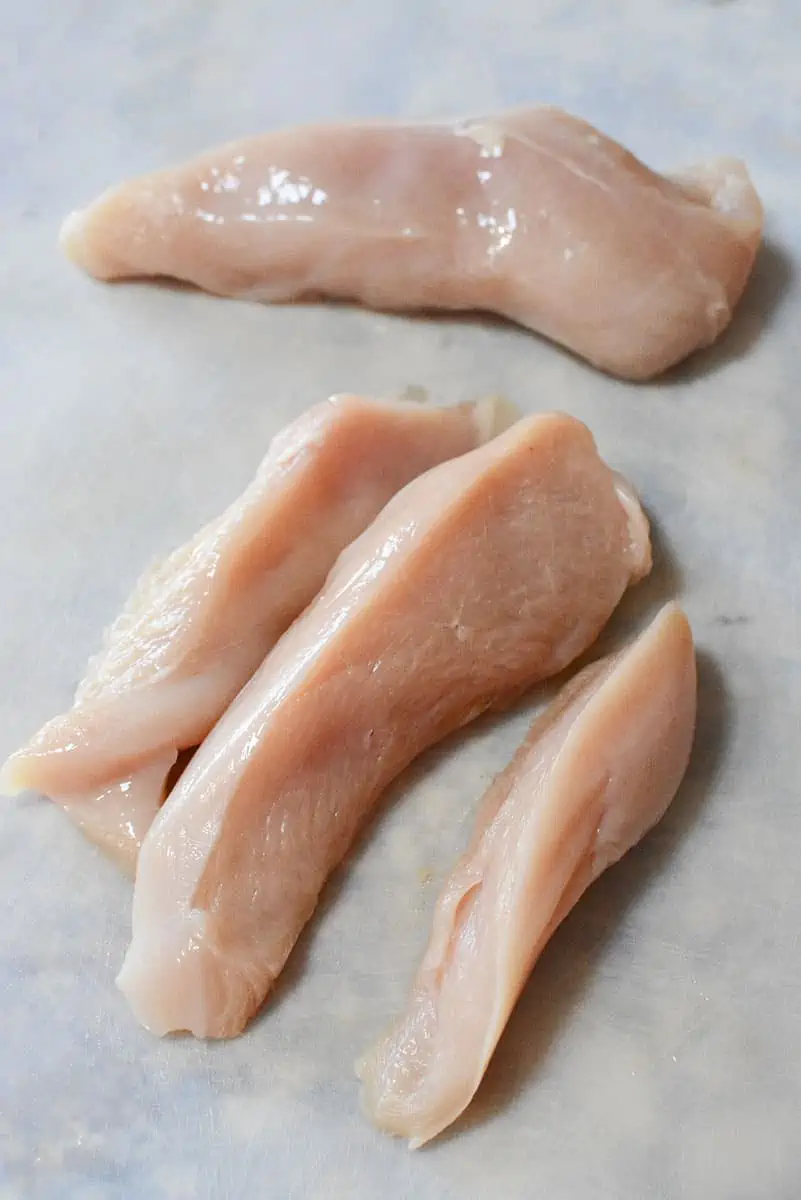 Chicken breasts cut into strips on a white cutting board.