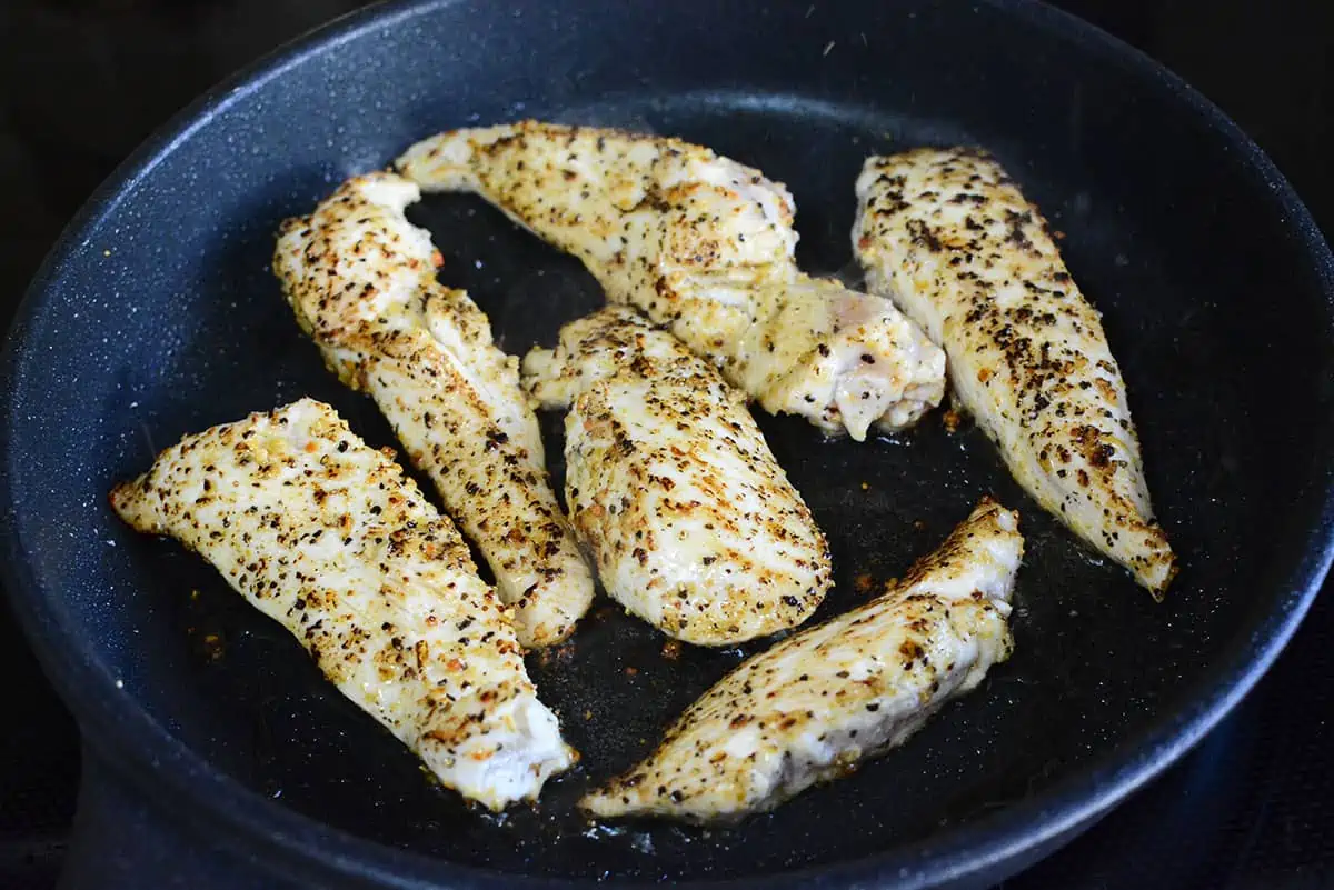 Searing the seasoned chicken strips in the skillet.