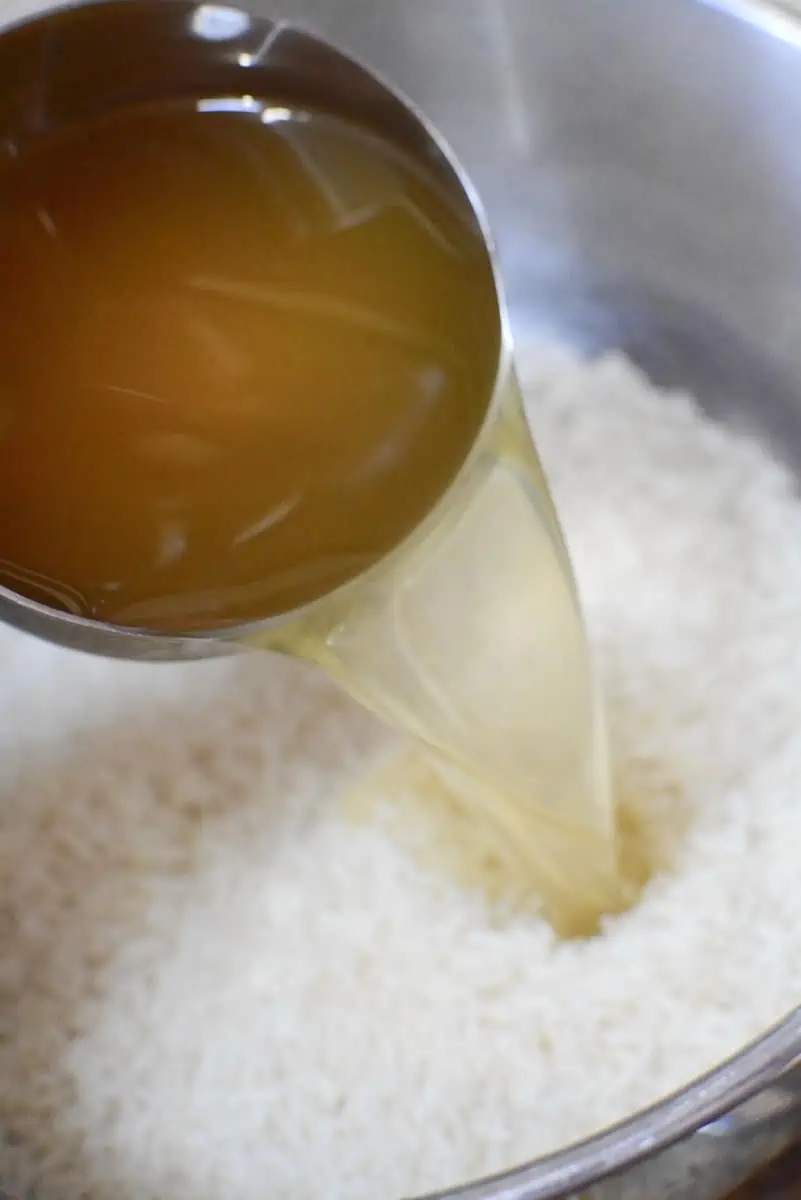 Adding chicken broth to the rice and soup mixture.