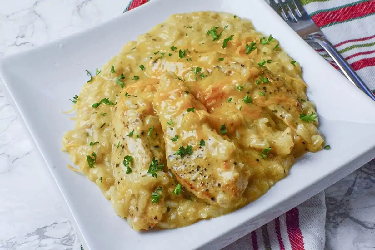 Slow cooker cheesy chicken risotto dinner with chicken pieces up front. A fork lies to the right of the white plate.