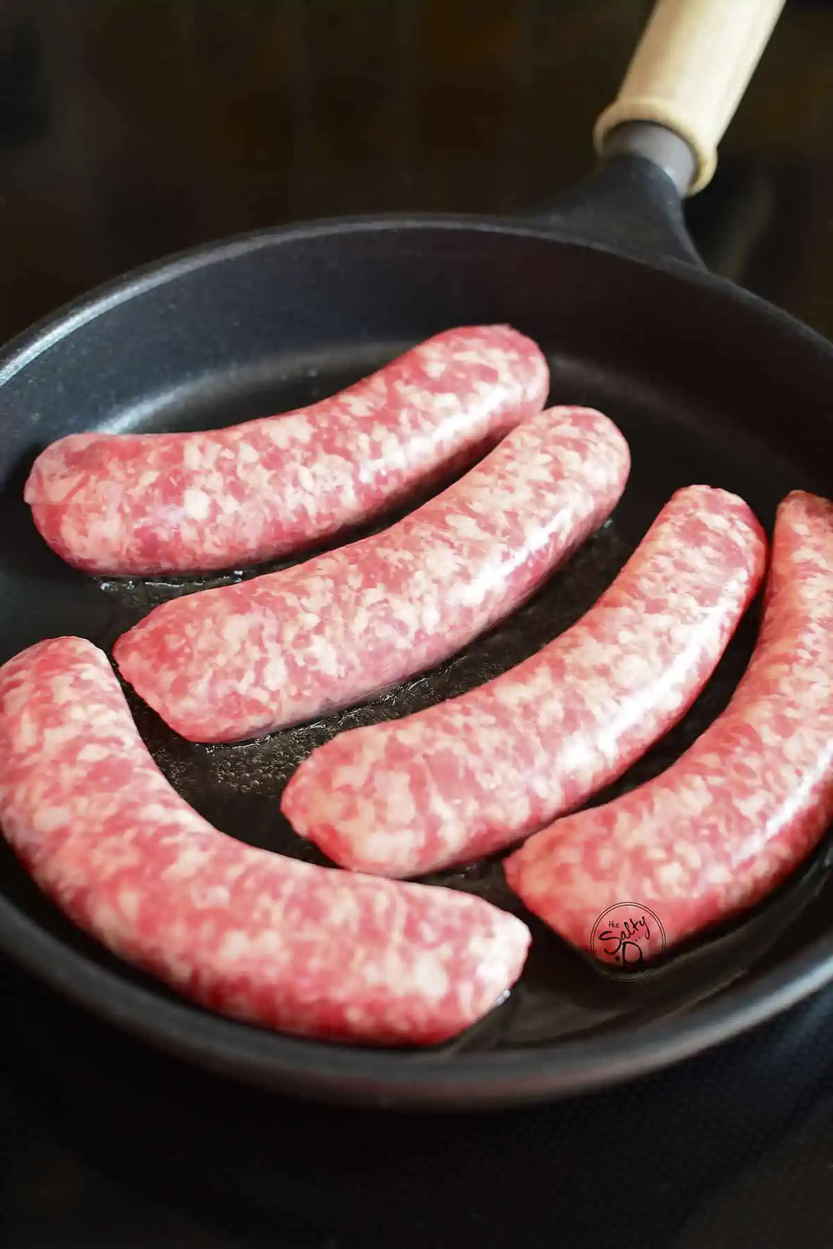 Five raw sausages in a skillet.