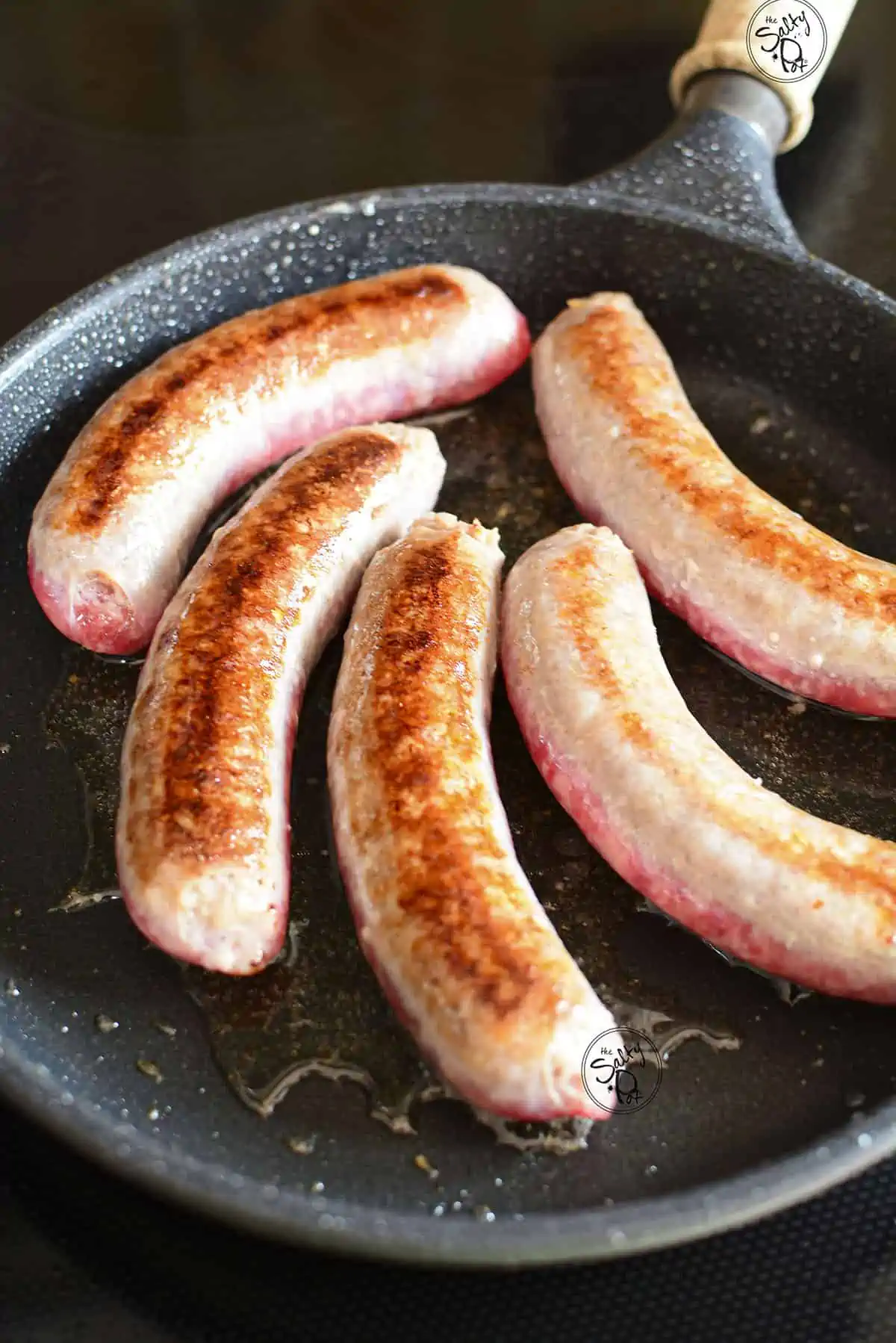 5 cooking bratwurst sausages in a cast iron skillet.