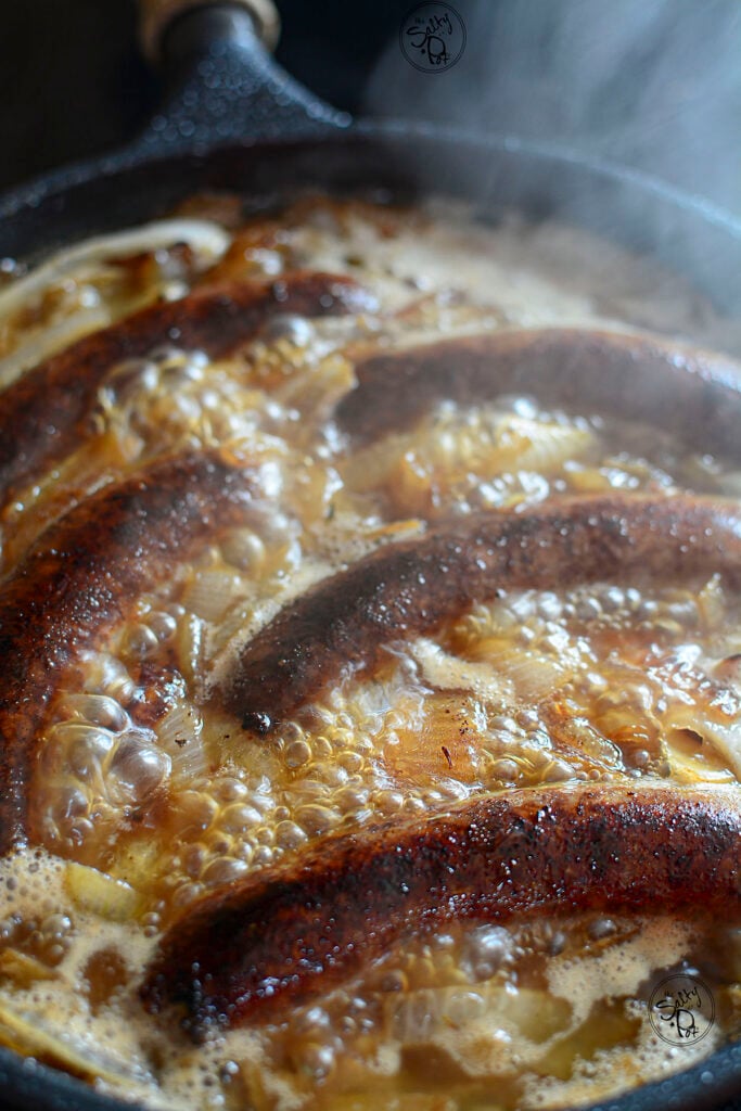 Caramelized onions and bratwurst in a skillet boiling to reduce the beer.