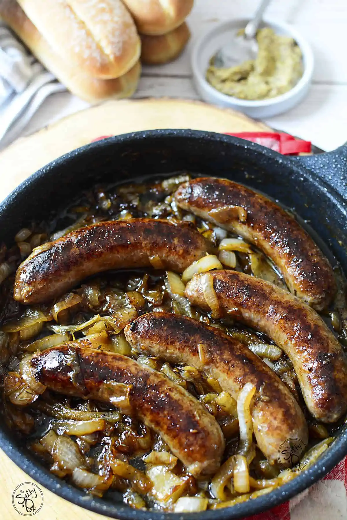 5 bratwurst sausages with onions in a cast iron skillet.