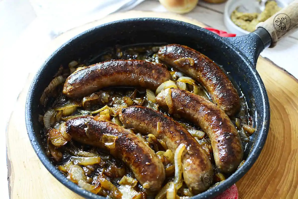 Five brats in a frying pan with caramelized onions. 