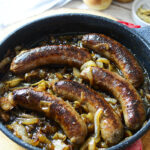 Five beer brats in a cast iron skillet with caramelized onions.