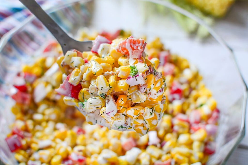 A spoonful of corn salad with bacon in a glass bowl.