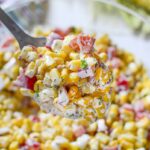 A spoonful of corn salad with bacon in a glass bowl.