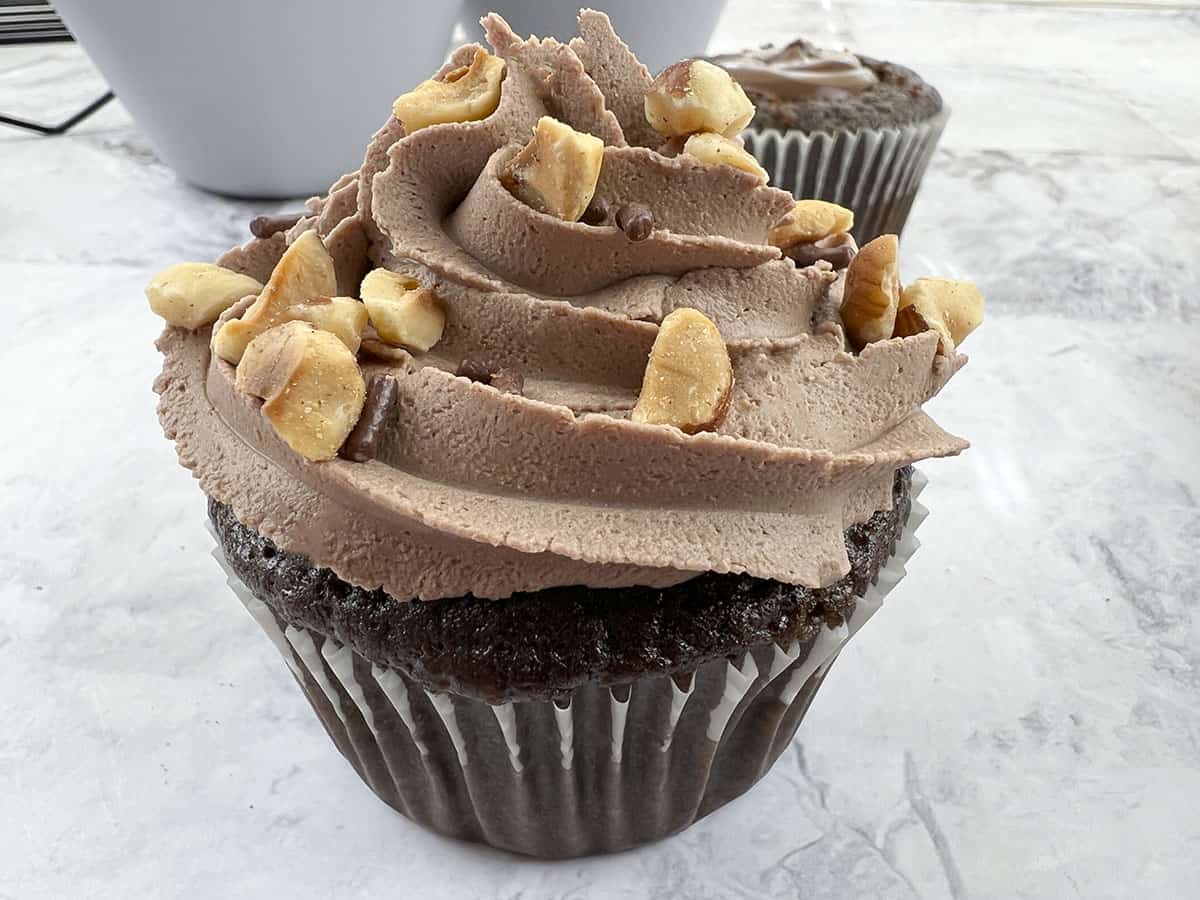 A frosted cupcake with hazelnuts sprinkled on top, waiting for the chocolate sprinkles.