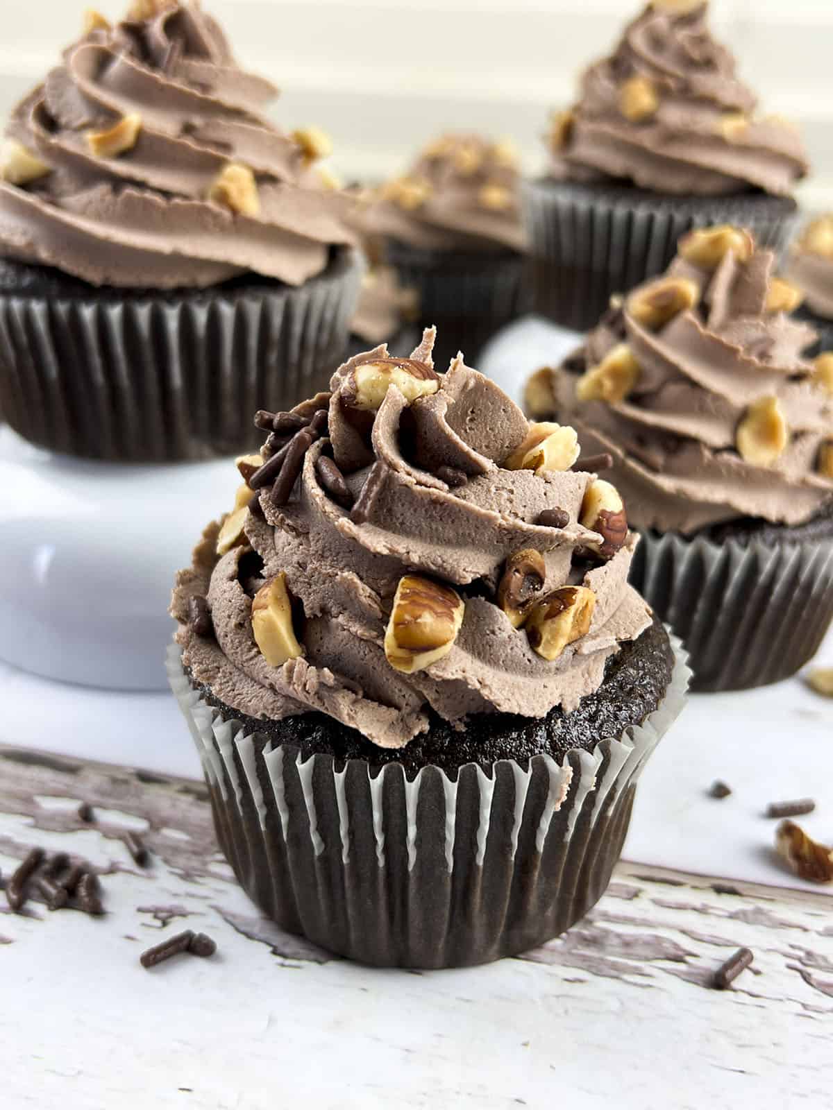 One nutella cupcake sits up front with other cupcakes in the back. The cupcake has nuts on the frosting.