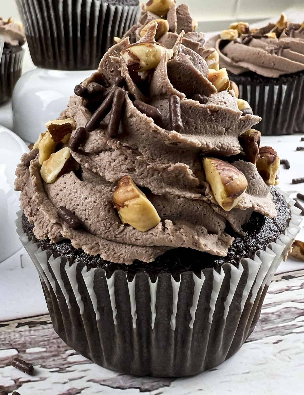 A close up photo of the cupcake with chocolate frosting and nuts.