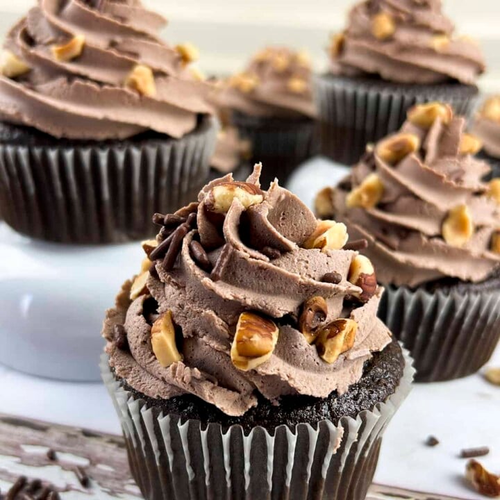 4 Nutella cupcakes with nuts and chocolate buttercream are sitting on different risers to give them height.