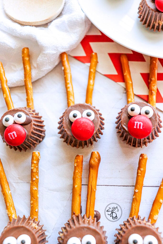 Thee rudolph candy treats with M&M noses are sitting on a white table above three other treats. 