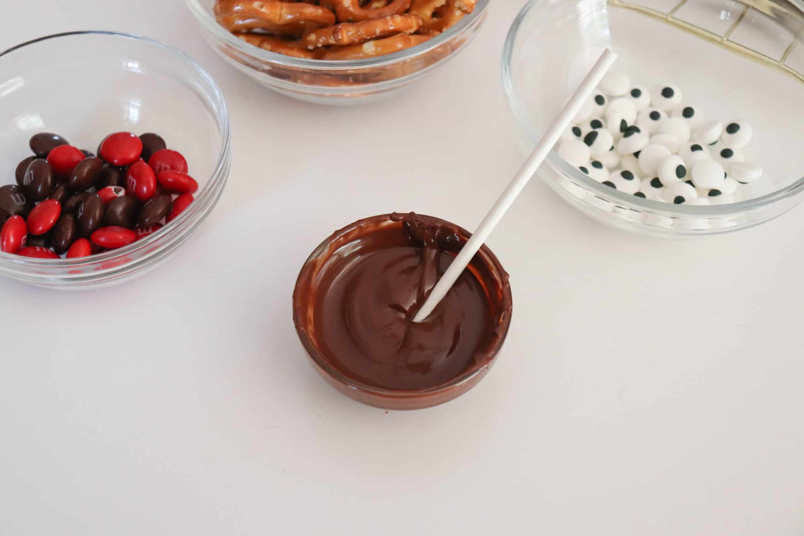 The chocolate chips are melted and ready to use for the 'glue'. MnM's are in a bowl to the left, pretzels at the top and candy eyes on the right.