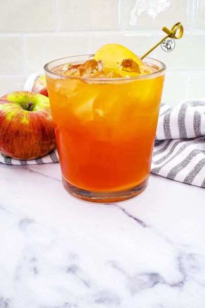Fireball Apple Cider Cocktail with apples in the background along with a striped napkin.