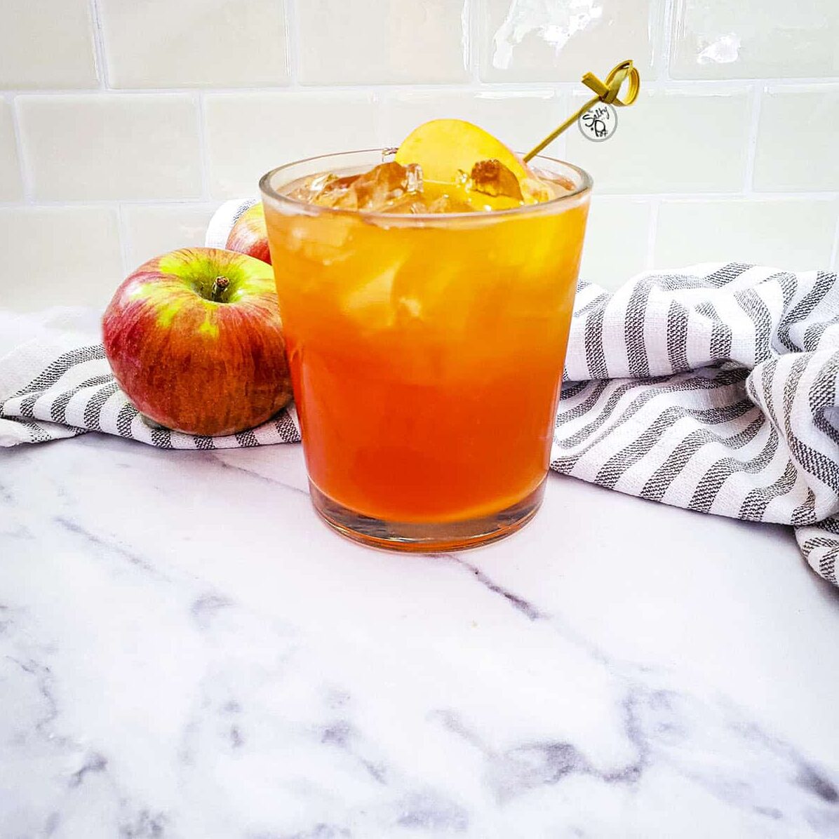 Fireball Apple Cider Cocktail with apples in the background along with a striped napkin.