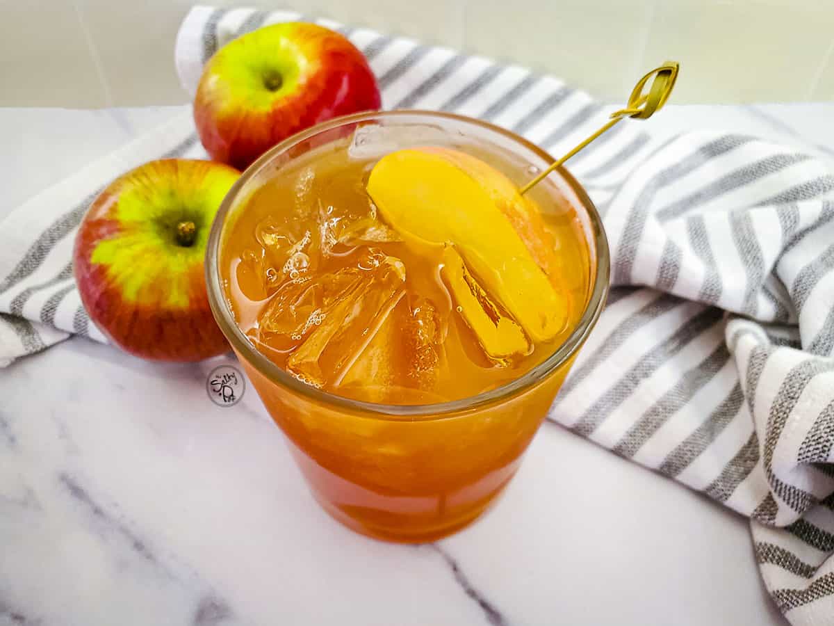 A top down photograph of the cinnamon cocktail. Two apples are on the top left. 