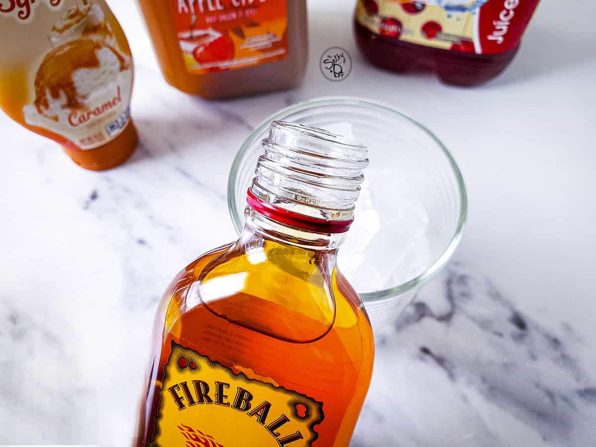 Adding the fireball whiskey to the glass with ice. The other ingredients are across the top of the photo.